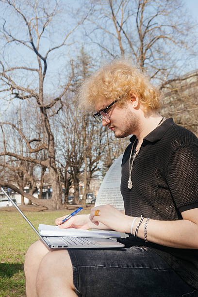 istock A focused student works outdoors on a laptop and takes notes while sitting alone on a park bench on a sunny day 2212813102