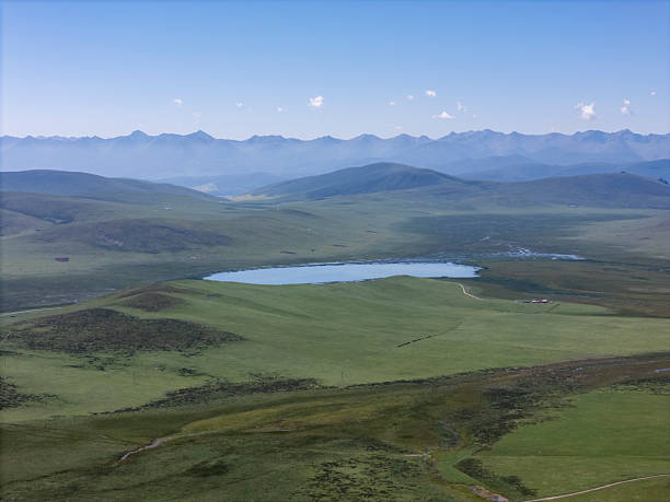 Scenic aerial view of rolling hills and a peaceful lake, ideal for nature photography or travel brochures. The lush greenery and clear blue sky create a calming visual experience.