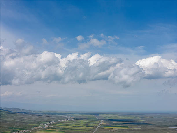 Panoramic aerial shot of a rural area with fields and roads, showcasing natural beauty and tranquility. The image captures the essence of open countryside with a mix of greenery and blue skies, offering a sense of peace and vastness. Potential usage includes travel brochures, nature documentaries, or environmental campaigns.