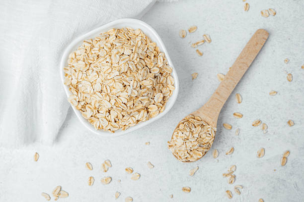 istock Oats in a bowl with a wooden spoon on a light textured surface 2212832451