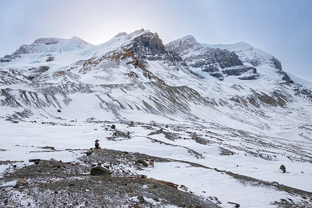 Towering mountains covered in snow rise majestically against a clear blue sky. Rocky terrain stretches in the foreground, creating a stark contrast with the pristine snow.