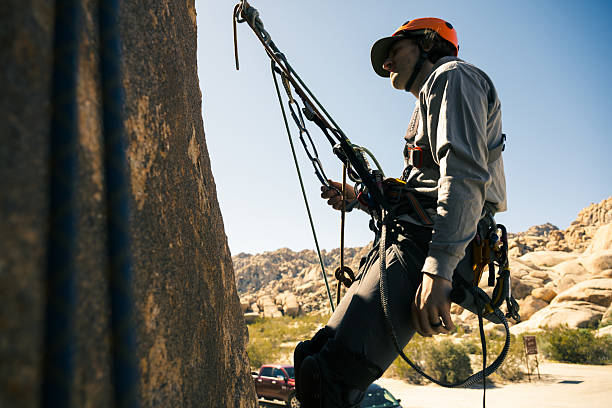 A climbing student completes their ascent and carefully attaches their personal safety system to the anchor at the top of the route. This technical moment emphasizes responsibility, self-reliance, and the mastery of adaptive climbing skills in a secure and inclusive outdoor setting.