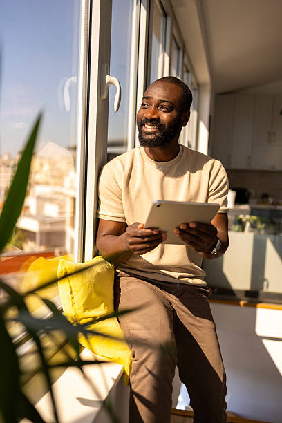 istock Smiling man sitting by a window and using a tablet in natural sunlight 2212847655