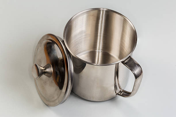 Stainless steel cup with handle and removed lid beside on a gray background