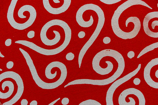 View of batik fabric featuring a dynamic swirling pattern in bright red and white. The bold, flowing lines and scattered dots create a visually striking and energetic textile design.
