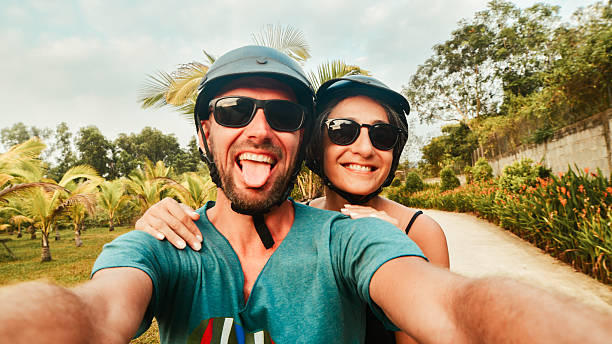 istock Portrait crazy smiley young happy caucasian couple take smartphone selfie while having fun driving scooter on tropical road trip in southeast asia. Couple in love having fun travel in asia 2212860433