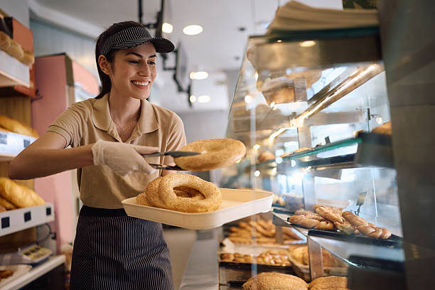 Happy female bakery worker arranging fresh pasty.