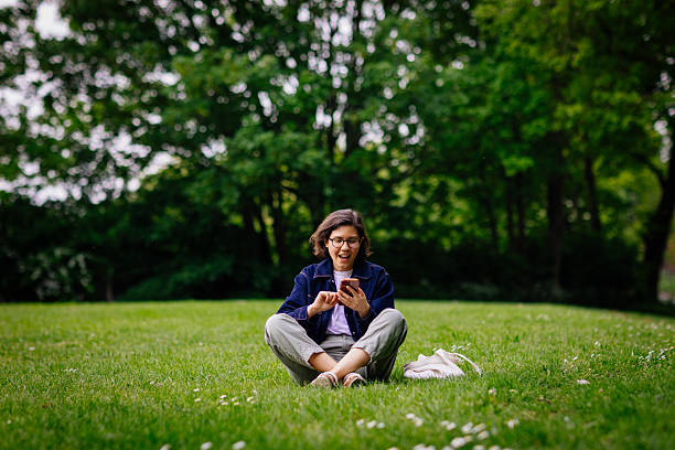 istock Cheerful female using phone sitting on grass 2212867258