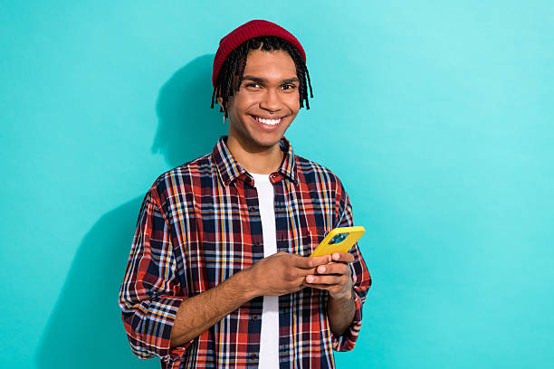 istock Photo of toothy beaming funny guy with cornrows dressed checkered shirt writing email on smartphone isolated on teal color background 2212867305