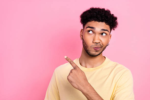 istock Photo interested young guy direct finger empty space unsure doubtful advertisement wear shirt isolated pink color background 2212870012