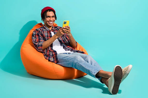 istock Full size photo of positive guy dressed checkered shirt jeans sit on pouf read post on smartphone isolated on teal color background 2212873241