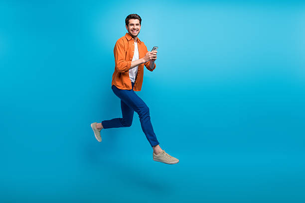 istock Full length profile portrait of handsome excited guy use smart phone jumping rush empty space isolated on blue color background 2212873920