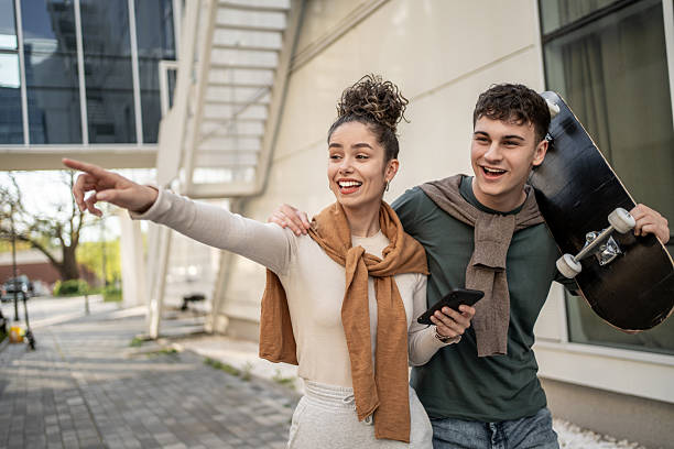 istock Young couple exploring city with skateboard and smartphone, pointing at something interesting 2212876700