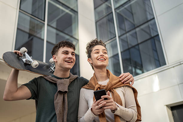 istock Smiling students looking up carrying skateboard and smartphone 2212877339
