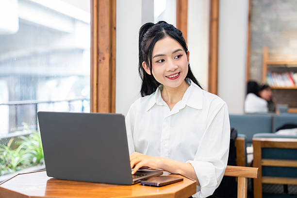 istock Smiling woman working on a laptop in a cafe by the window enjoying her day while working 2212881486