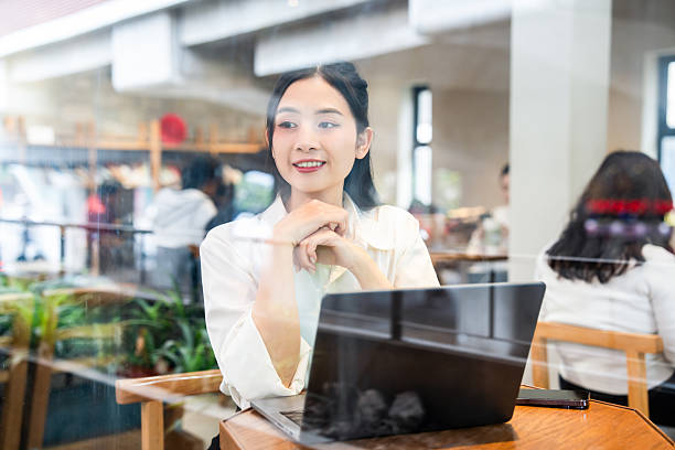 istock Young professional works on laptop in cafe setting seen through the window with a smile 2212881915