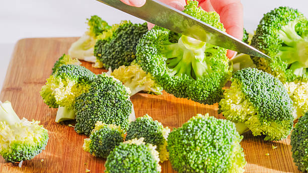 istock Knife cutting through broccoli florets on a wooden cutting board. 2212884358