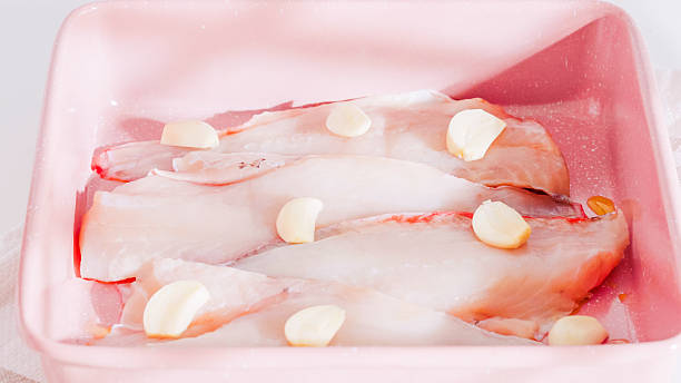 istock Raw fish fillets with garlic cloves in a pink baking dish. 2212884364