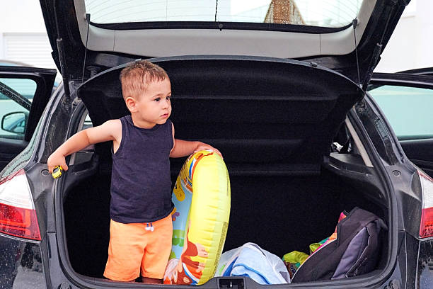 istock A young boy stands inside an open car trunk holding a swim ring, ready for vacation. 2212888910
