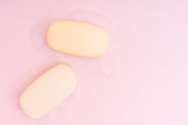 Two bars of soap with foam on a pink background.