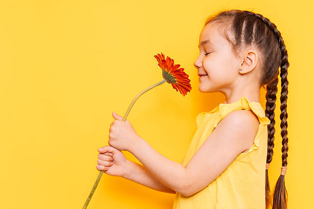 Child smells a red flower against a yellow background.