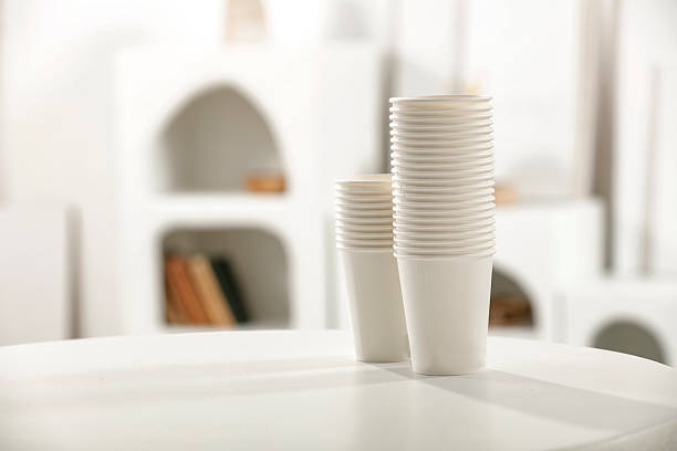 White paper cups placed on a light table in a sunlit modern interior with minimalist furniture. The bright, airy space evokes calm summer mornings, slow living, and elegant home lifestyle. Ideal for wellness, interior design, or morning rituals concepts.