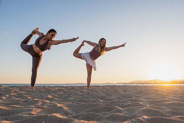 istock Two women practicing yoga poses on the beach at sunset 2212906106