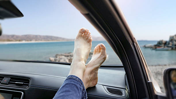 istock Legs resting on the car dashboard on the beach - summer road trip lifestyle. Empty space for branding product or text placement. 2212907171