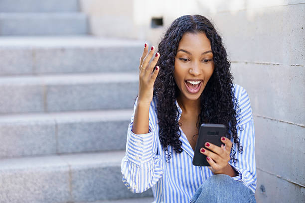 istock A young and enthusiastic woman is happily engaging with her smartphone while sitting on the steps 2212908844