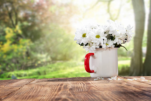Wooden table with a mug with white flowers with copy space. Spring or summer outdoor background. Nice rural landscape in rustic style.