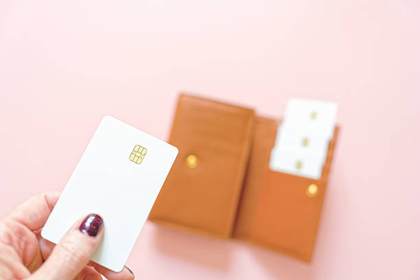 Woman with blank credit card paying bill and brown leather wallet on pink surface in background - woman paying with blank credit card - banking concept, finance, financial health