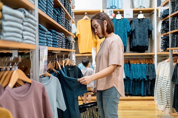 istock Female shopper browsing clothing rack, selecting trendy items while young son smiling beside her in retail boutique 2212925562