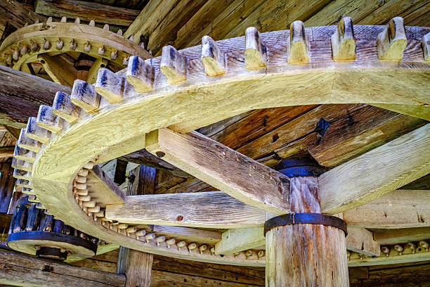Close-up of large metallic gears engaged in a mechanical process, highlighting intricate design and functionality. Sunlight casts shadows, emphasizing the textures and precision of the machinery.