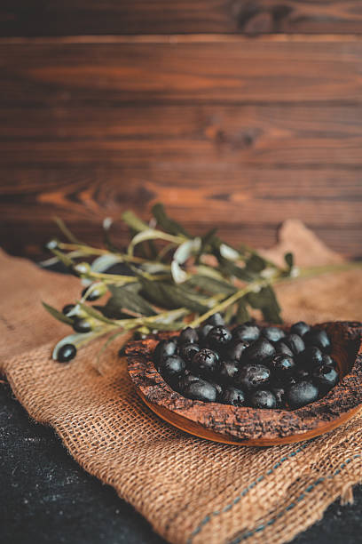 istock Rustic wooden bowl filled with glossy black olives on a burlap surface, with olive branches in the background. Warm natural light, traditional Mediterranean food concept 2212929358
