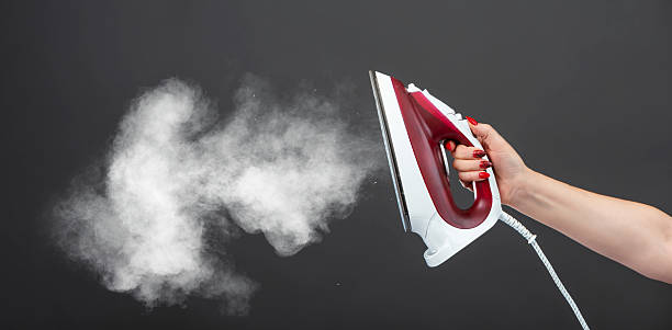 istock Woman holds an iron with steam on gray background 2212935821