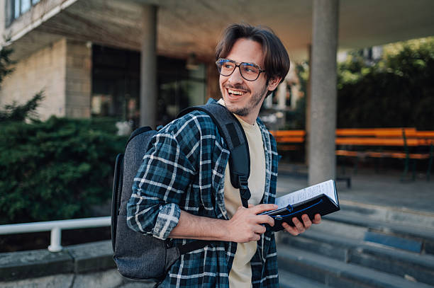 istock Smiling student walking outside university building holding a book 2212940321