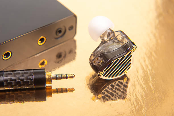 istock An earbud, a 3.5mm audio jack, and a black audio device on a gold surface, great for showcasing tech accessories and sound equipment. 2212951145
