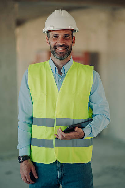 istock Smiling engineer holding tablet wearing hardhat and safety vest at construction site 2212954644