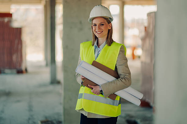 istock Female architect smiling and holding blueprints on construction site 2212954656