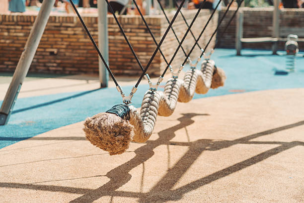Close-up view of a row of thick rope pendulums hanging diagonally on metal cables at a modern outdoor playground with soft rubber flooring and warm natural sunlight; Punta Umbria, Spain