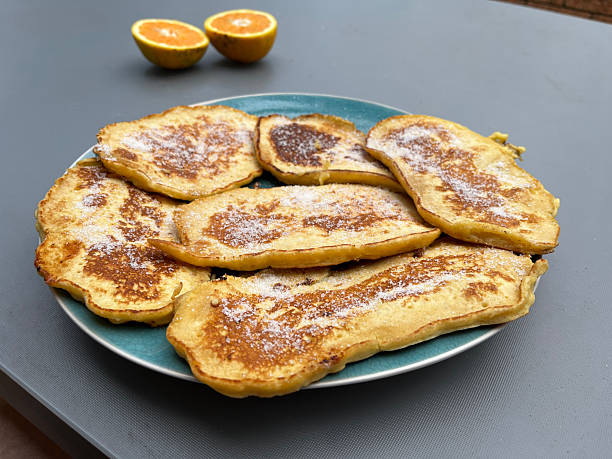 A plate filled with golden pancakes, lightly sprinkled with sugar and drizzled with fresh orange juice