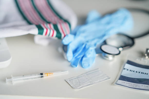 Various medical tools including gloves, a stethoscope, a syringe, and identification card are neatly displayed on a white table, representing healthcare preparation and organization.