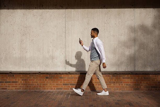 istock Man Walking Outdoors Holding Phone Near Concrete Wall on a Sunny Day 2212966182