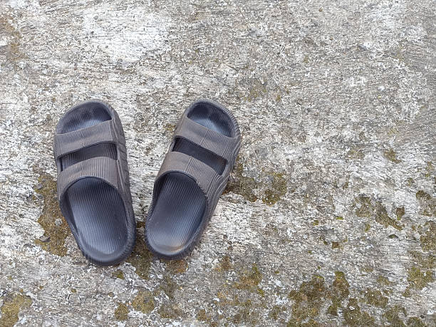 Old shabby sandals, broken slippers on top with sand background, worn and damaged black leather slippers