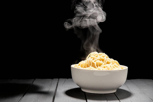 Ready-to-eat noodles in a white bowl placed on a kitchen table, isolated on a black background.