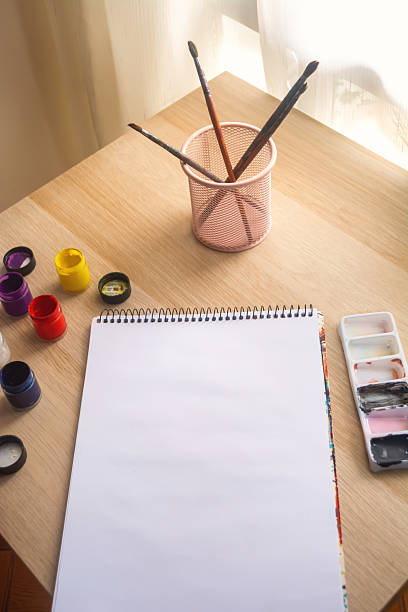 istock Blank Sketchpad with Paints and Brushes on Wooden Desk 2212971825