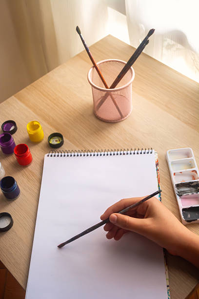 istock Hand Holding Brush Above Blank Sketchpad for Painting 2212971836