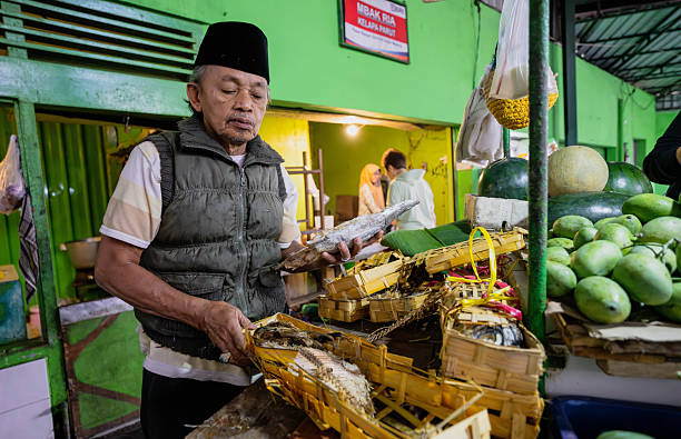 Malang, Indonesia - July 27, 2024 :  This photograph captures a moment at a lively market in Malang, Indonesia, where a vendor displays fresh fish amidst the sights and sounds of local trade.