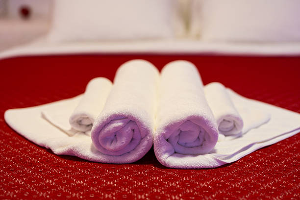 Fresh white towels are arranged on a red bedspread with a decorative flower adding charm.