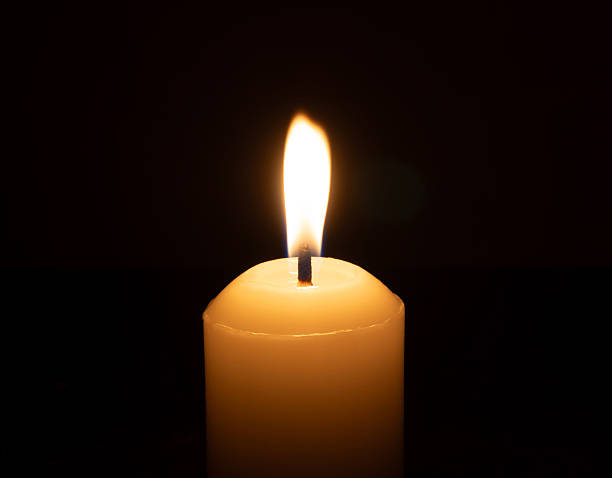 istock A single burning candle flame or light glowing on a big white candle isolated on black or dark background on table in church for Christmas, funeral or memorial service 2212986223